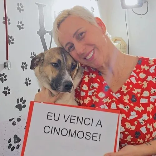 Cão com a placa “Eu venci a cinomose!” ao lado da Dra. Cris